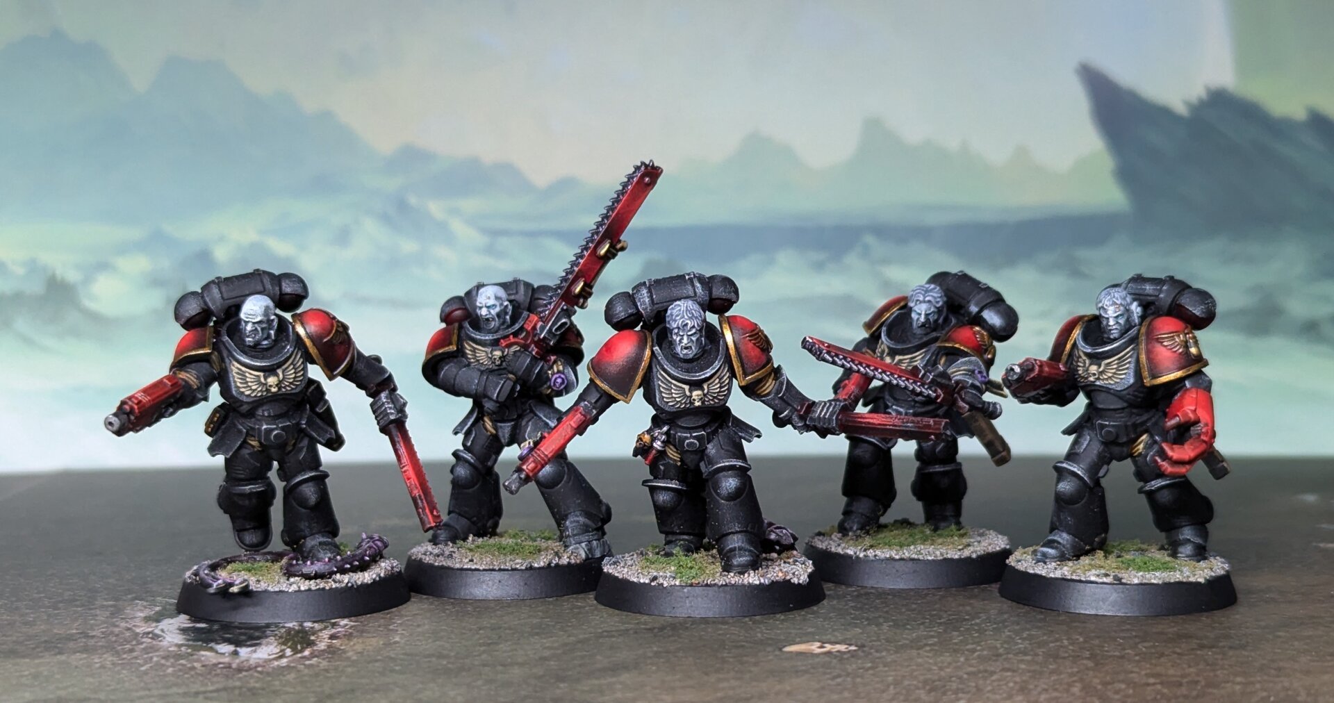 A photograph of five painted Warhammer 40,000 miniaturs. Black power armor with red and gold accents. The heads are in black and white.