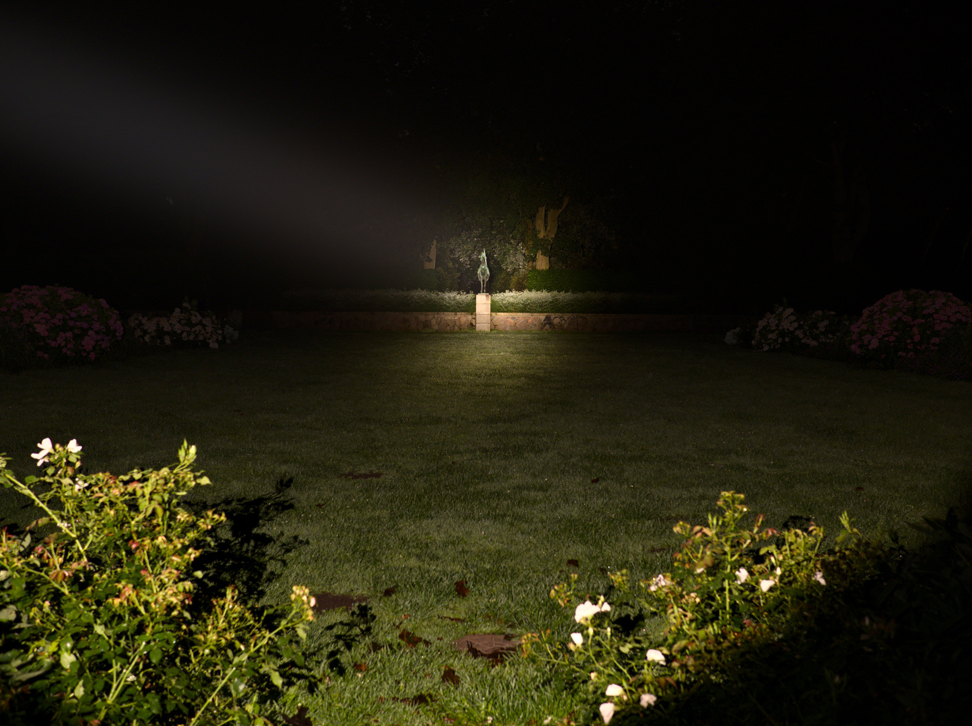 A focused flashlight beam with warm color temperature illuminates a distant statue